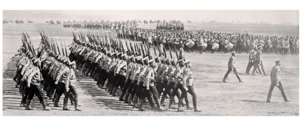 Black and white photo of Russian Infantry soldiers in uniform marching in formation with rifles and bayonets on an open field during a military parade.