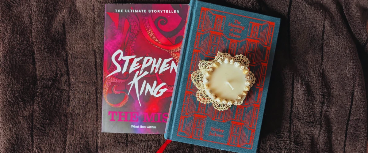 Two horror books, "The Mist" by Stephen King and "The Haunting of Hill House" by Shirley Jackson, with a candle placed on the latter.